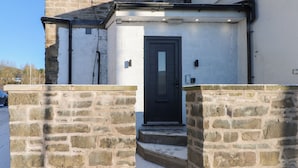 A stone-walled building with a black door and a small set of steps leading to a white door. - The Penthouse at 86 (Rossendale)