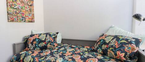 A bedroom with a bed, floral-patterned bedding, a wall art piece, and a bedside lamp.