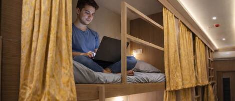 A bunk bed with a laptop, wooden walls, and yellow curtains.