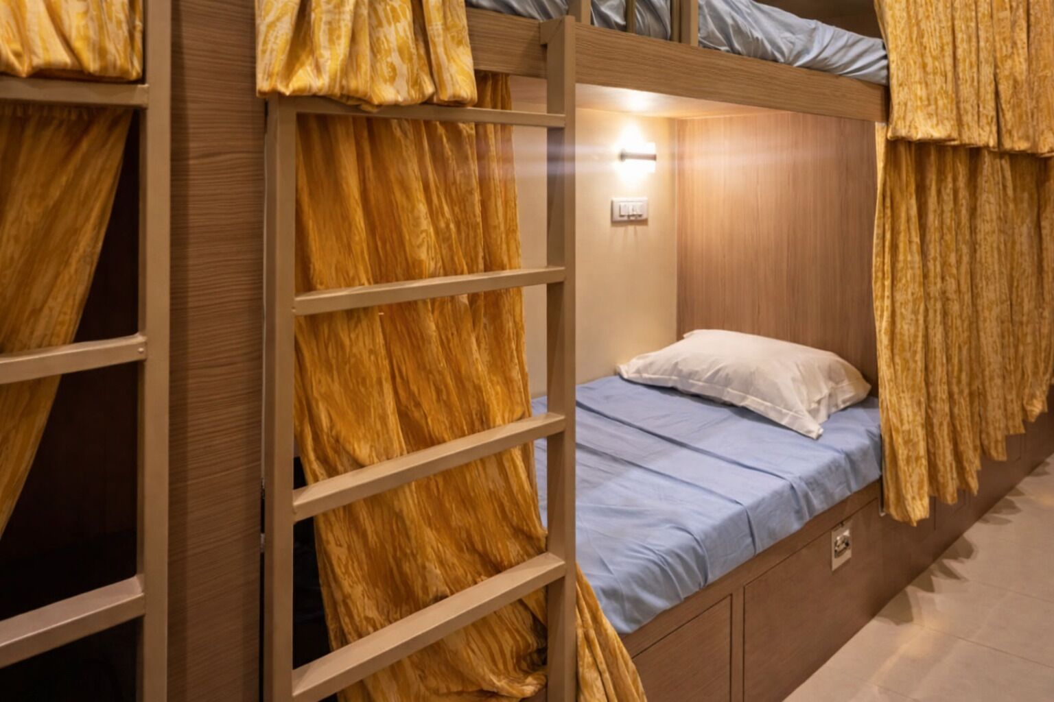 Un lit superposé avec un matelas bleu et un oreiller blanc, une tête de lit en bois et un luminaire au-dessus du lit.