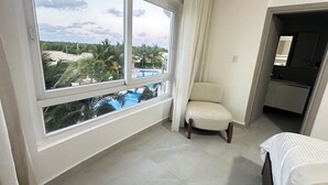 A hotel room with a large window, a chair, a bed, and a small kitchenette. - Caribbean 2BR Apartment - Facing the pool (Punta Cana)