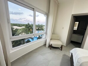 Ein Hotelzimmer mit großem Fenster, einem Sessel, einem Bett und einer kleinen Küchenzeile.