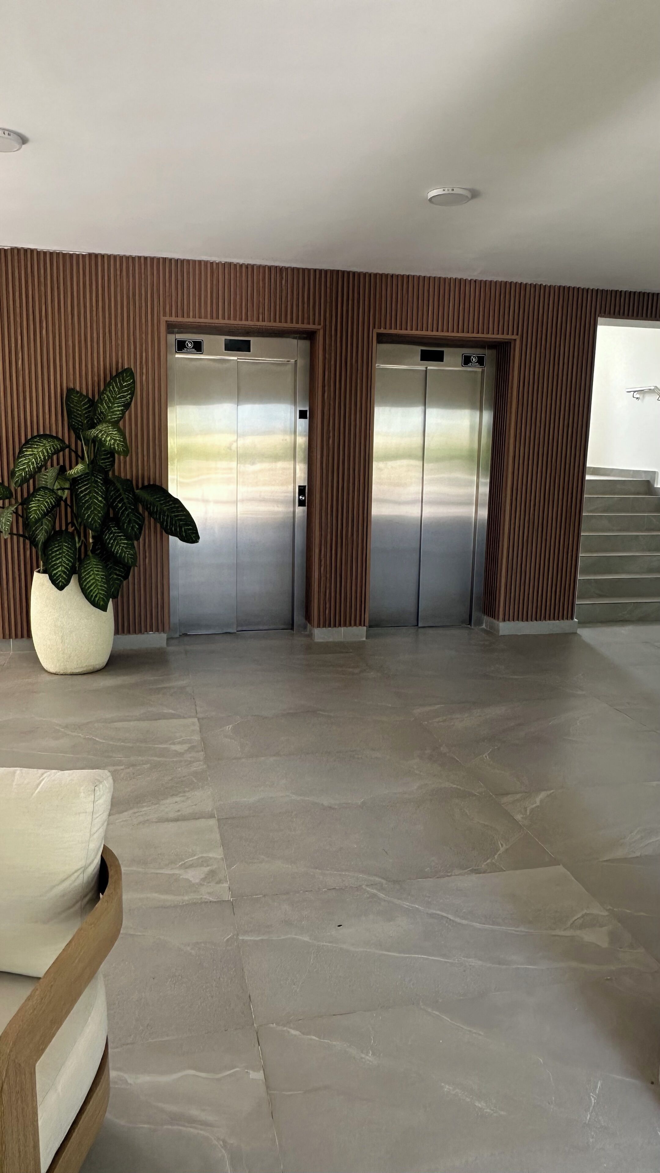 A spacious lobby with two elevators, a potted plant, and a staircase.