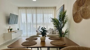 A modern dining area with a wooden table, woven placemats, and a sofa. - Caribbean 2BR Apartment - Facing the pool (Punta Cana)