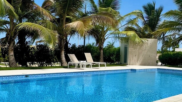 A swimming pool with lounge chairs and palm trees. - Caribbean 2BR Apartment - Facing the pool (Punta Cana)