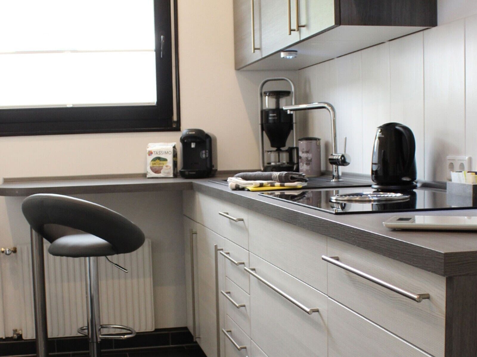 A modern kitchen with a coffee maker, kettle, and a bag of Tassimo pods.