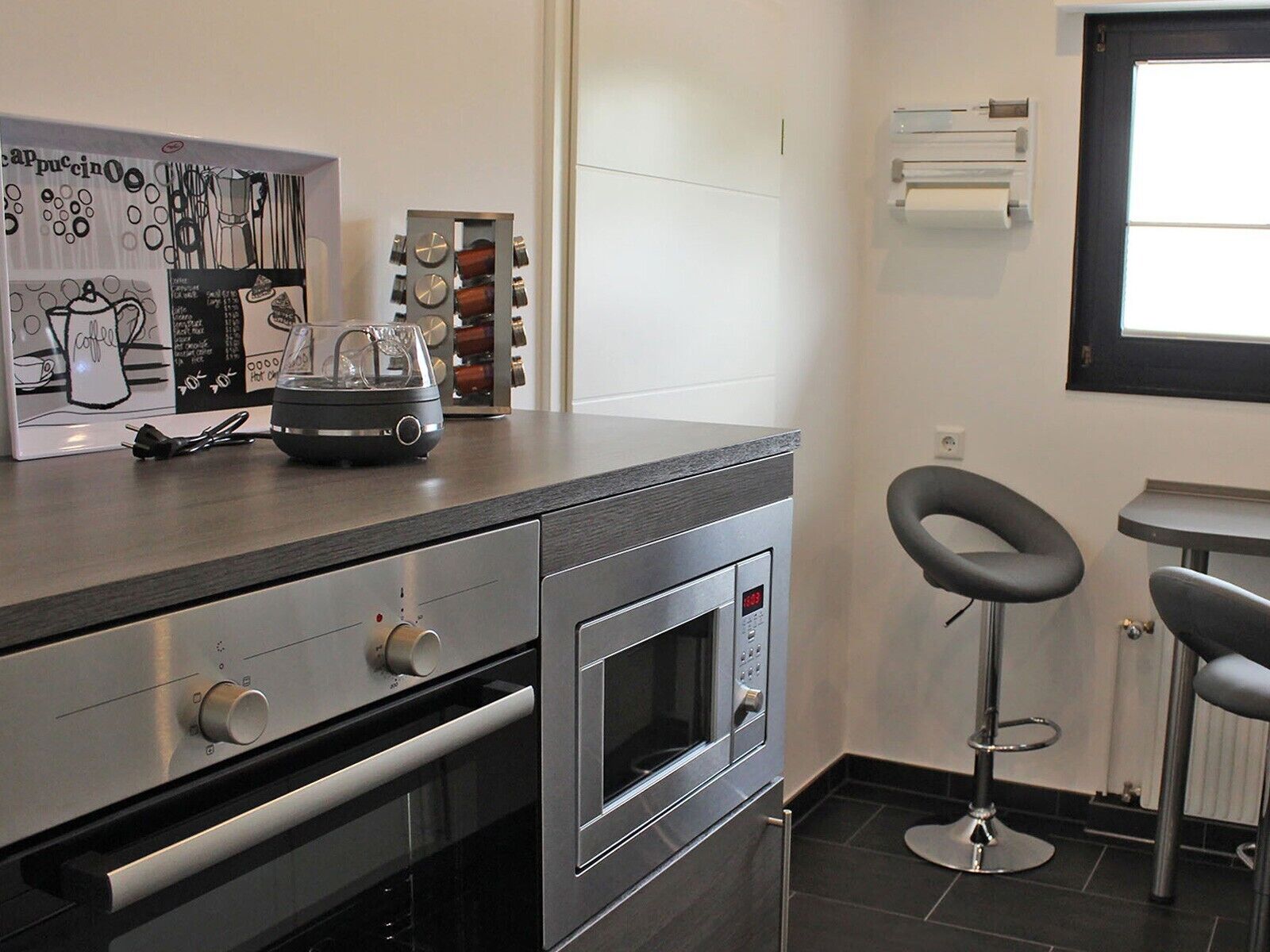 A modern kitchen with a built-in oven, a coffee machine, and a bar stool.