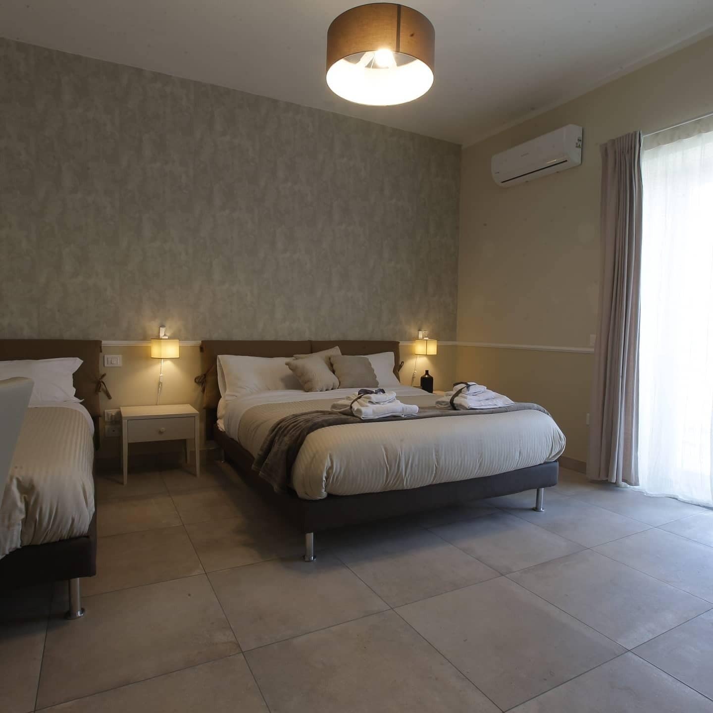 Hotelkamer met een groot bed, twee nachtkastjes, een wandairconditioner en een raam met gordijnen.