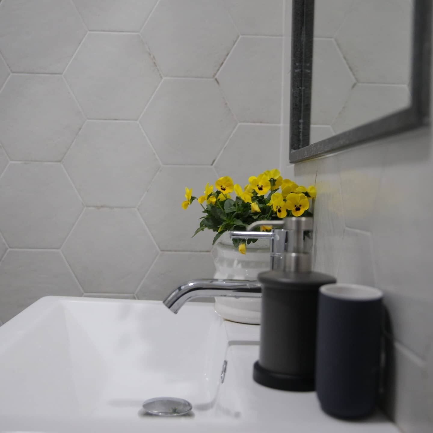 Een badkamer met een wit wastafelmeubel, een spiegel en een wand betegeld met hexagontegels.