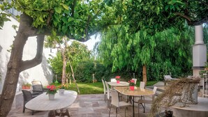 A patio with a round table and chairs, surrounded by lush greenery and a hanging plant. - B&B Maison de Charme (Pompei)