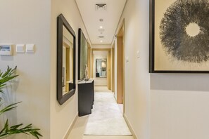 A hallway with a white carpet, a black vanity, and a large abstract painting on the wall. - Balcony-Facing Pool 2BR w/ Asst Room, Minutes Walk to Park and Miracle Garden (Dubai)