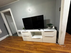 Un moble blanc de televisió amb un televisor de pantalla plana, calaixos i una petita planta.