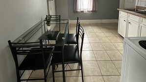 A compact kitchen with white cabinets, a dining table with chairs, a ceiling fan, and a window with curtains. - 2 Bedroom Cozy Accomodation (Windsor)