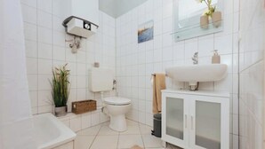 Une salle de bain moderne avec des carreaux blancs, des toilettes, un lavabo avec un meuble, une baignoire et une petite plante.