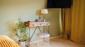 Une pièce comprenant une commode en bois, une plante en pot, un tabouret rond, une lampe et un téléviseur fixé au mur.