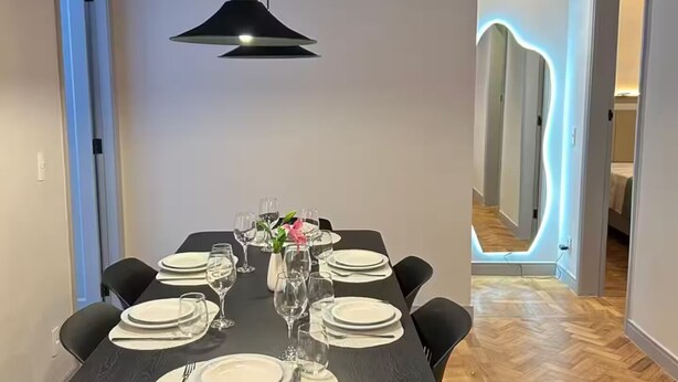 Ein Essbereich mit einem dunklen Holztisch, gedeckten Plätzen für sechs Personen, schwarzen Stühlen und einer schwarzen Pendelleuchte.