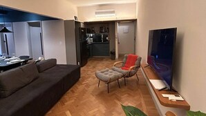 Ein modernes Wohnzimmer mit Sofa, Fernseher und Essbereich mit Tisch und Stühlen.