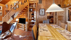 Ein Holzinnenraum mit Treppe, Essbereich mit Tisch und Stühlen, Fernseher und Regalen mit unterschiedlichen Gegenständen.