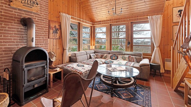 Ein gemütliches Blockhaus-Interieur mit Kamin, Sitzecke und großen Fenstern.