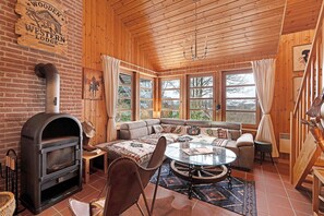 Un intérieur chaleureux de chalet avec une cheminée, un coin salon et de grandes fenêtres.