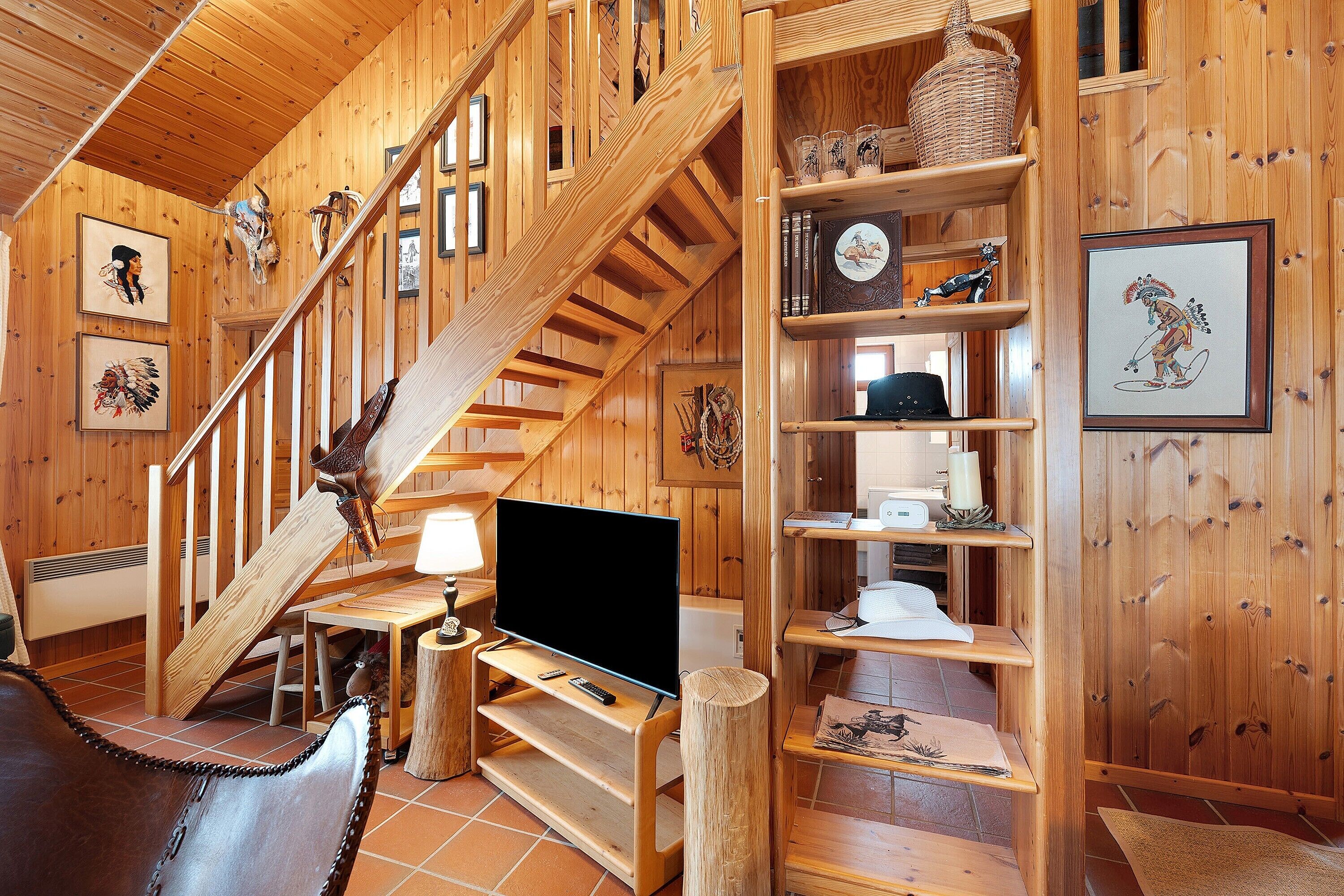 Un interior de madera con una escalera, un televisor de pantalla plana y estanterías con diversos objetos.