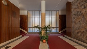Un couloir avec un tapis rouge, des murs lambrissés, une colonne centrale et une plante en pot.