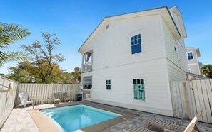Ein zweistöckiges weißes Haus mit Swimmingpool, Holzterrasse und Gartenmöbeln.