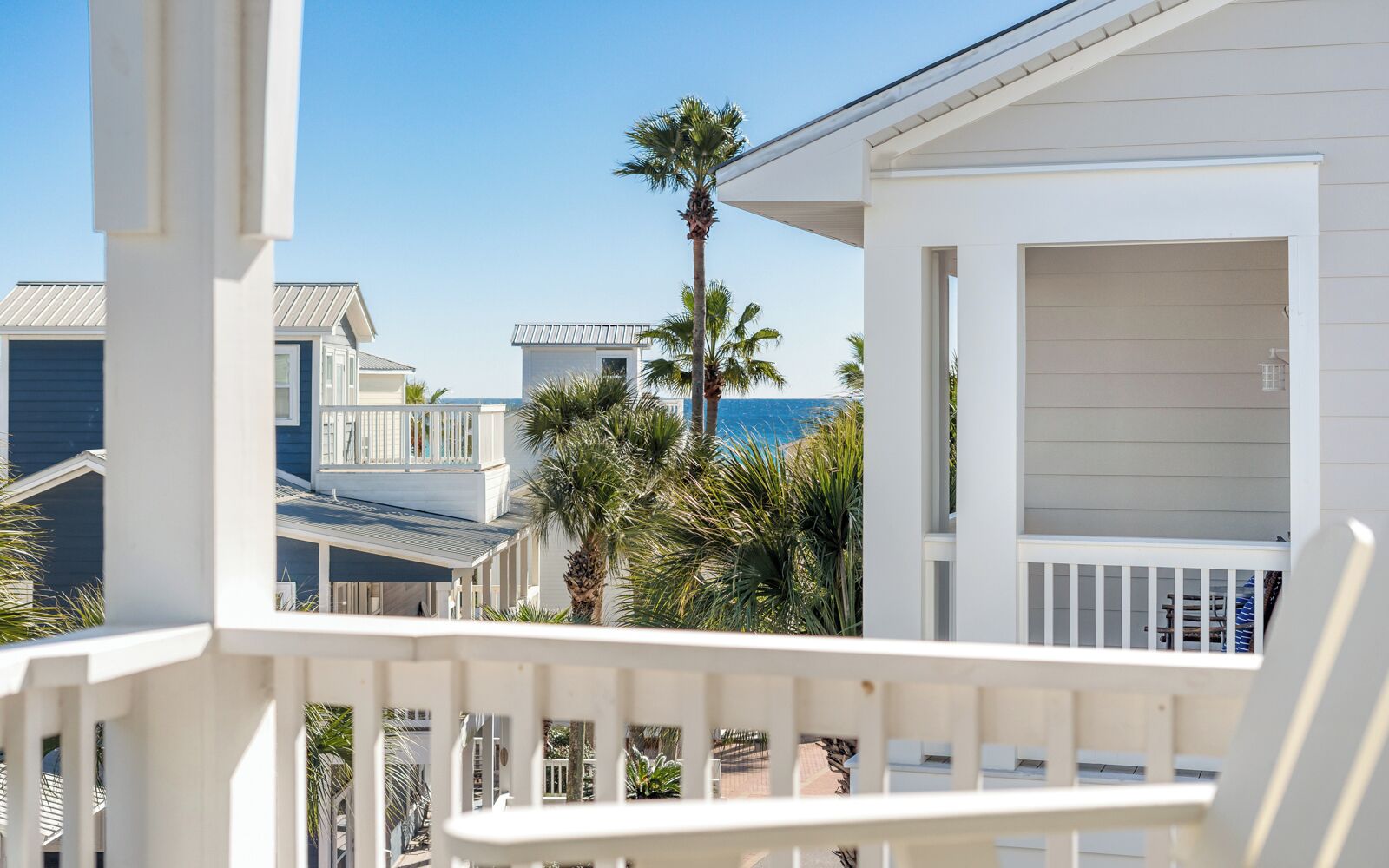 Une propriété située en bord de mer, dotée d’un balcon, de palmiers et offrant une vue sur l’océan.