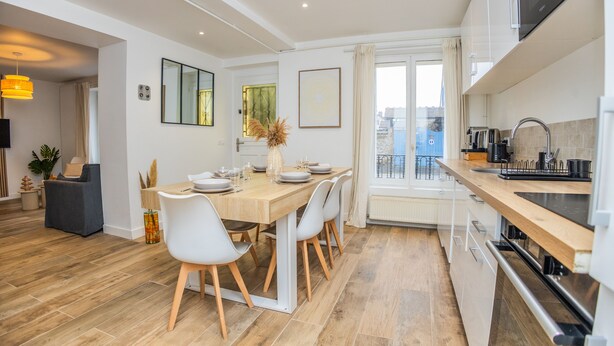 A modern kitchen with a dining area, wooden flooring, and a view of the city.