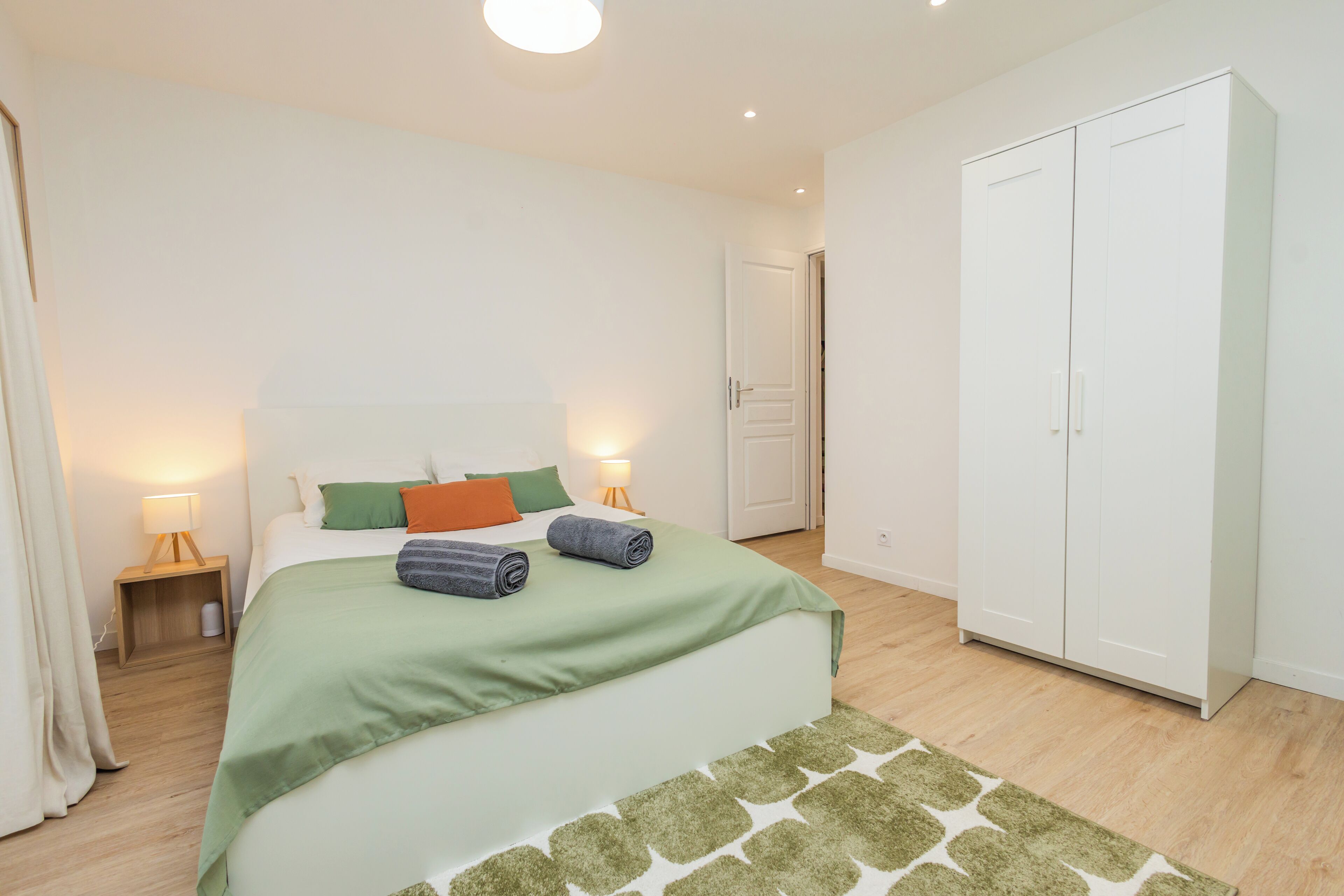 A bedroom with a bed, bedside tables, a wardrobe, and a door.