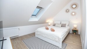 A bedroom with a skylight, a bed with pillows, a bedside table with a lamp, and a radiator.