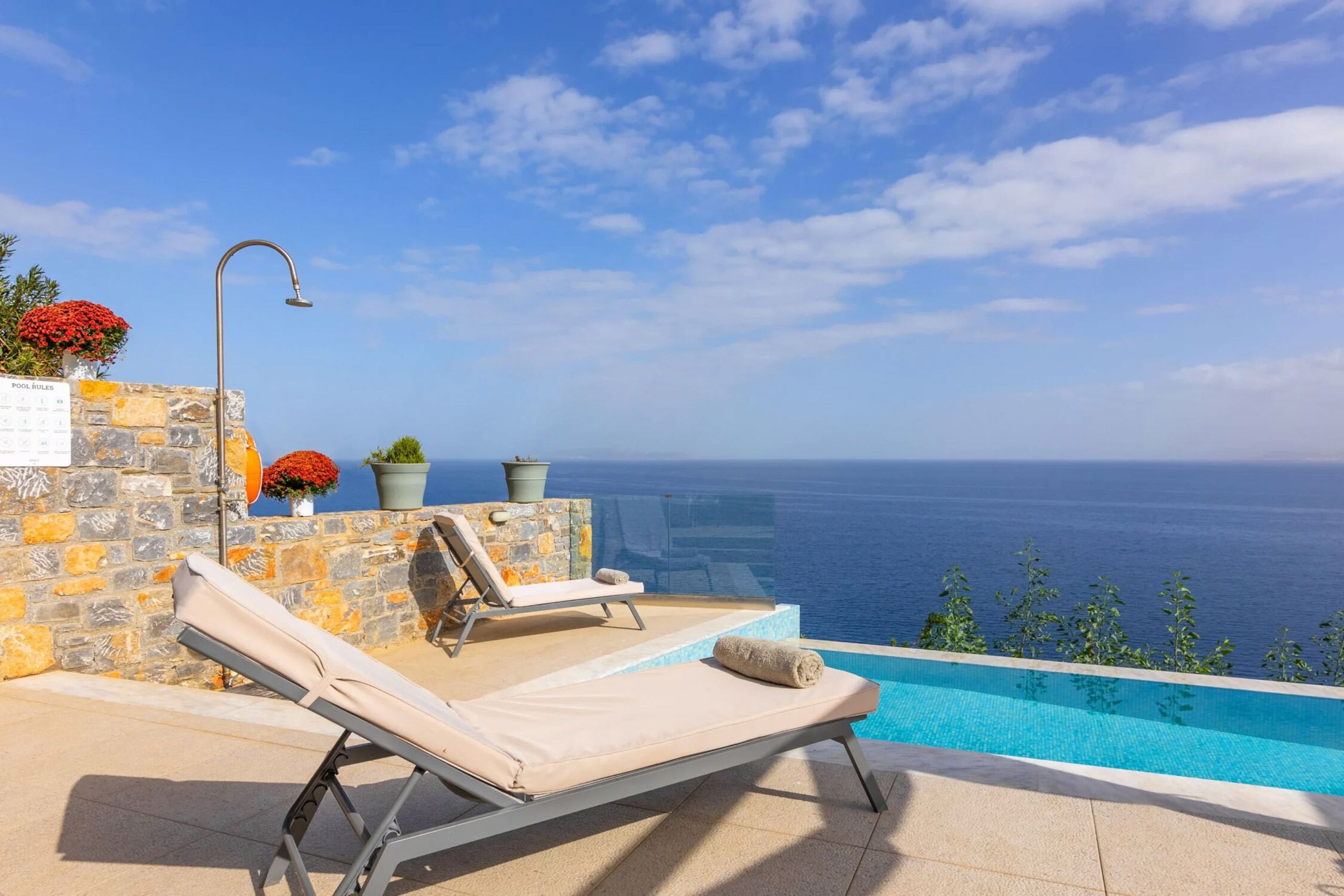 Un espace aménagé au bord de la piscine, avec une chaise longue, un mur en pierre et une vue sur la mer.