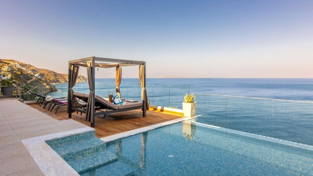 Een luxe buiten-infinitiezwembad met een houten terras, een hemelbed en uitzicht op de oceaan.