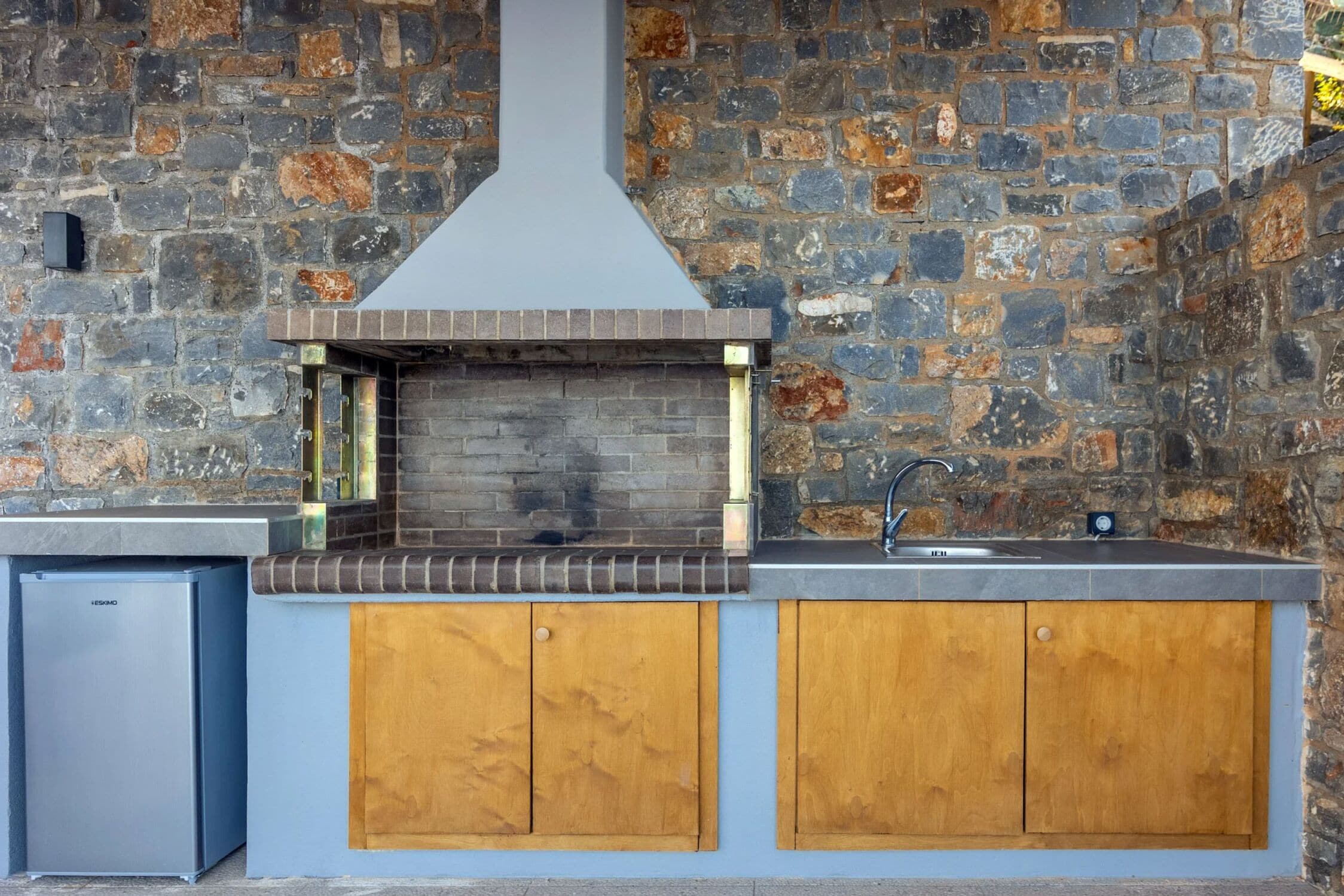 A kitchen with a stone wall, a built-in grill, and wooden cabinets.