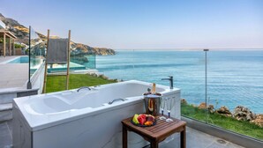 Een moderne badkamer met een ruime badkuip, een douche met glazen wand en uitzicht op zee.