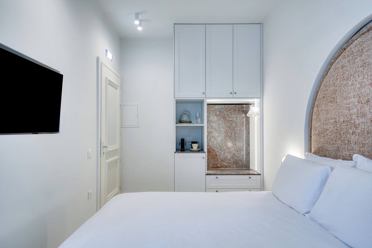 Un dormitorio con cama, un armario, una repisa con una tetera y un televisor instalado en la pared.