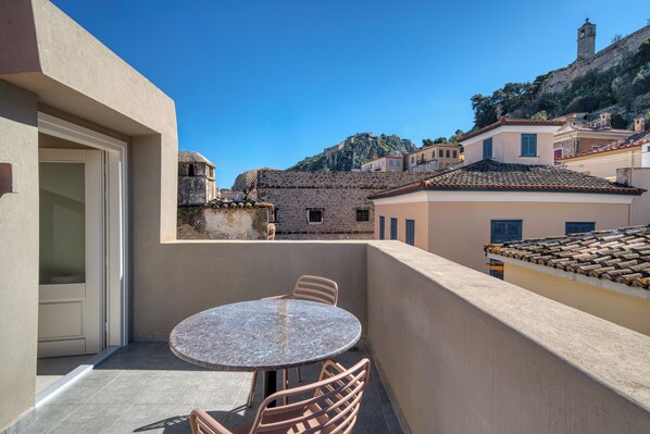 A balcony with a round table and chairs, overlooking a historic town with buildings and a hill. - Nalia Suites (Nafplio)