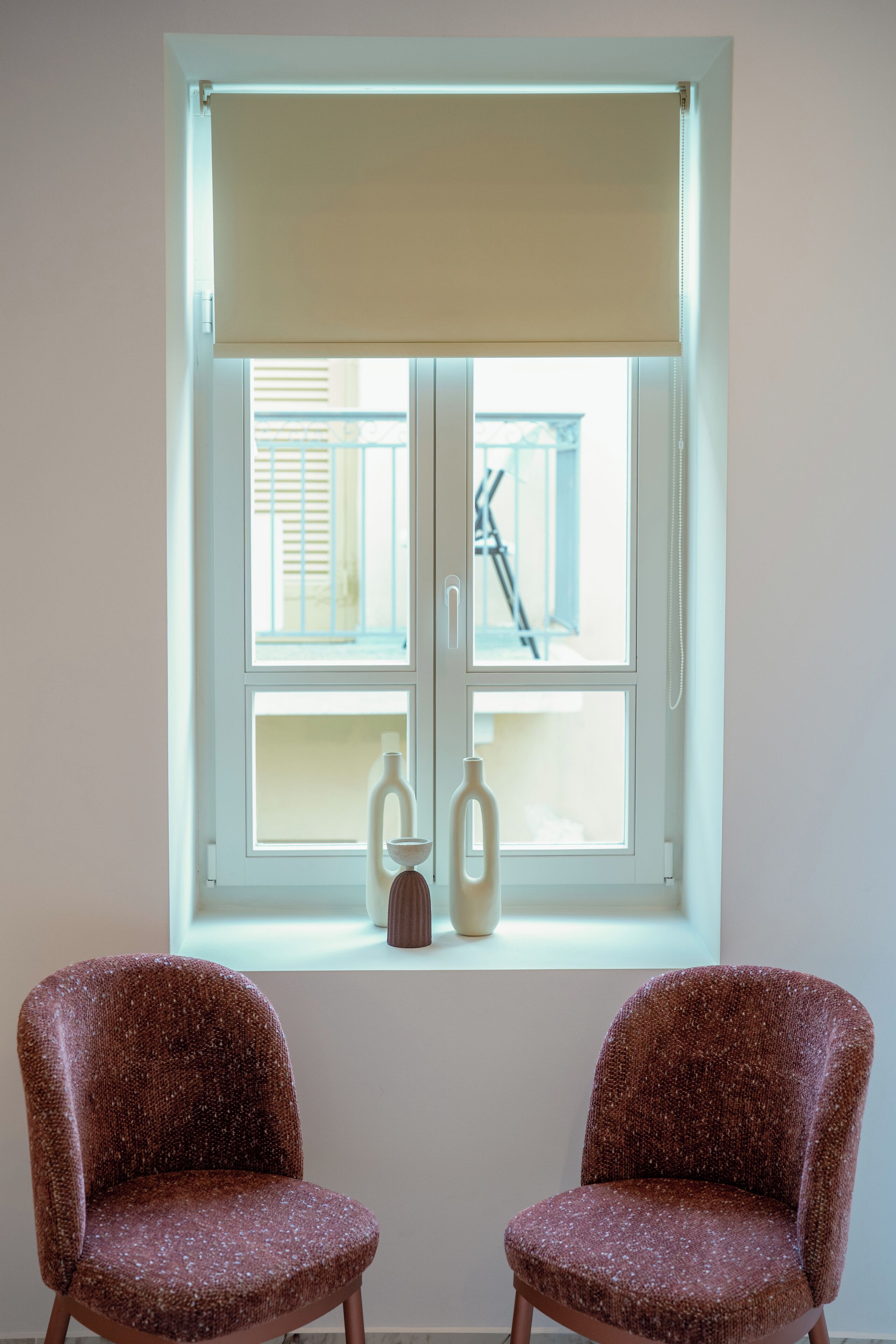 A room with a window, two chairs, and two vases on the windowsill.
