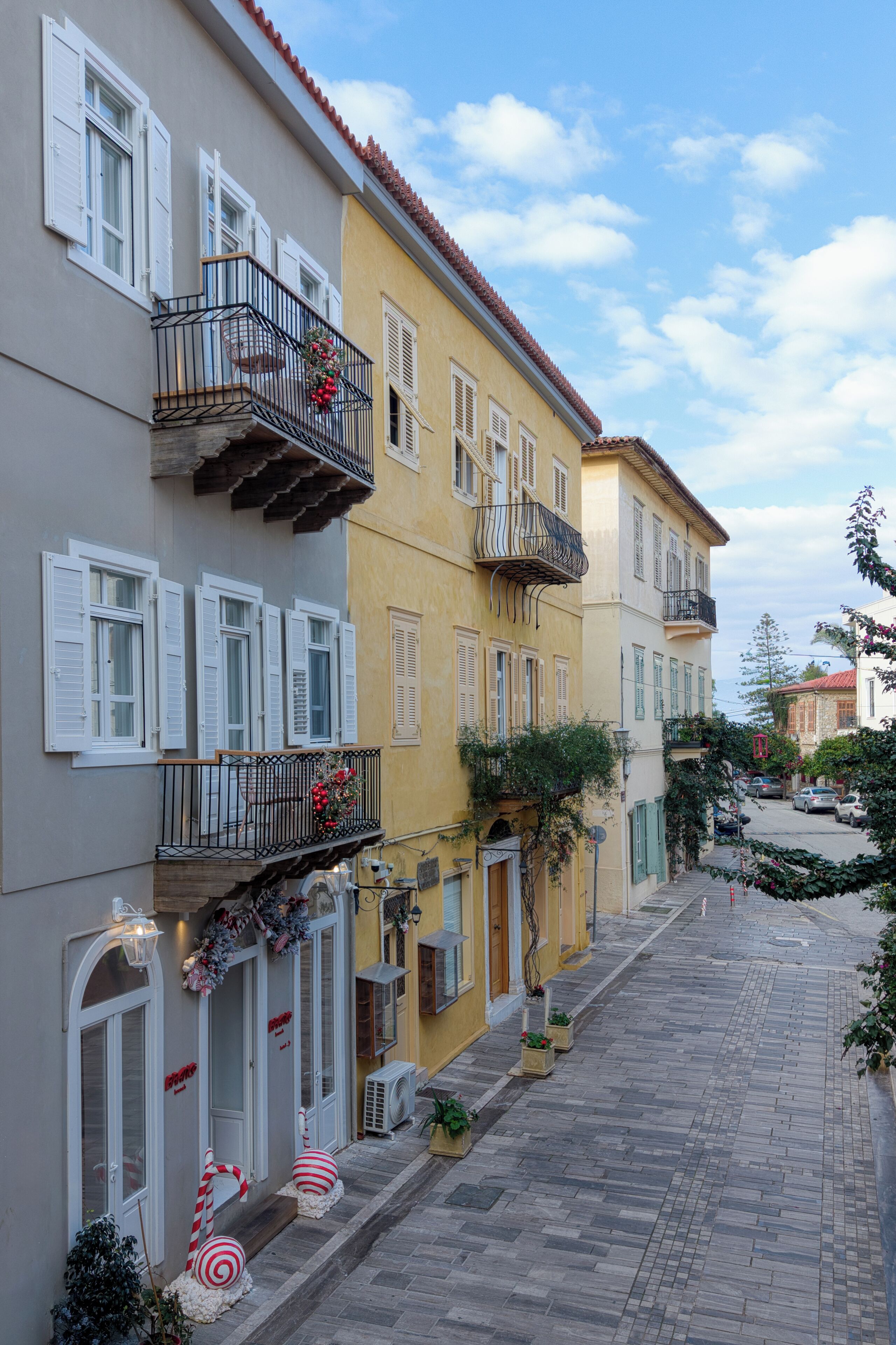 Una estrecha calle empedrada bordeada por edificios de varios pisos con balcones, algunos con barandillas y arreglos florales.