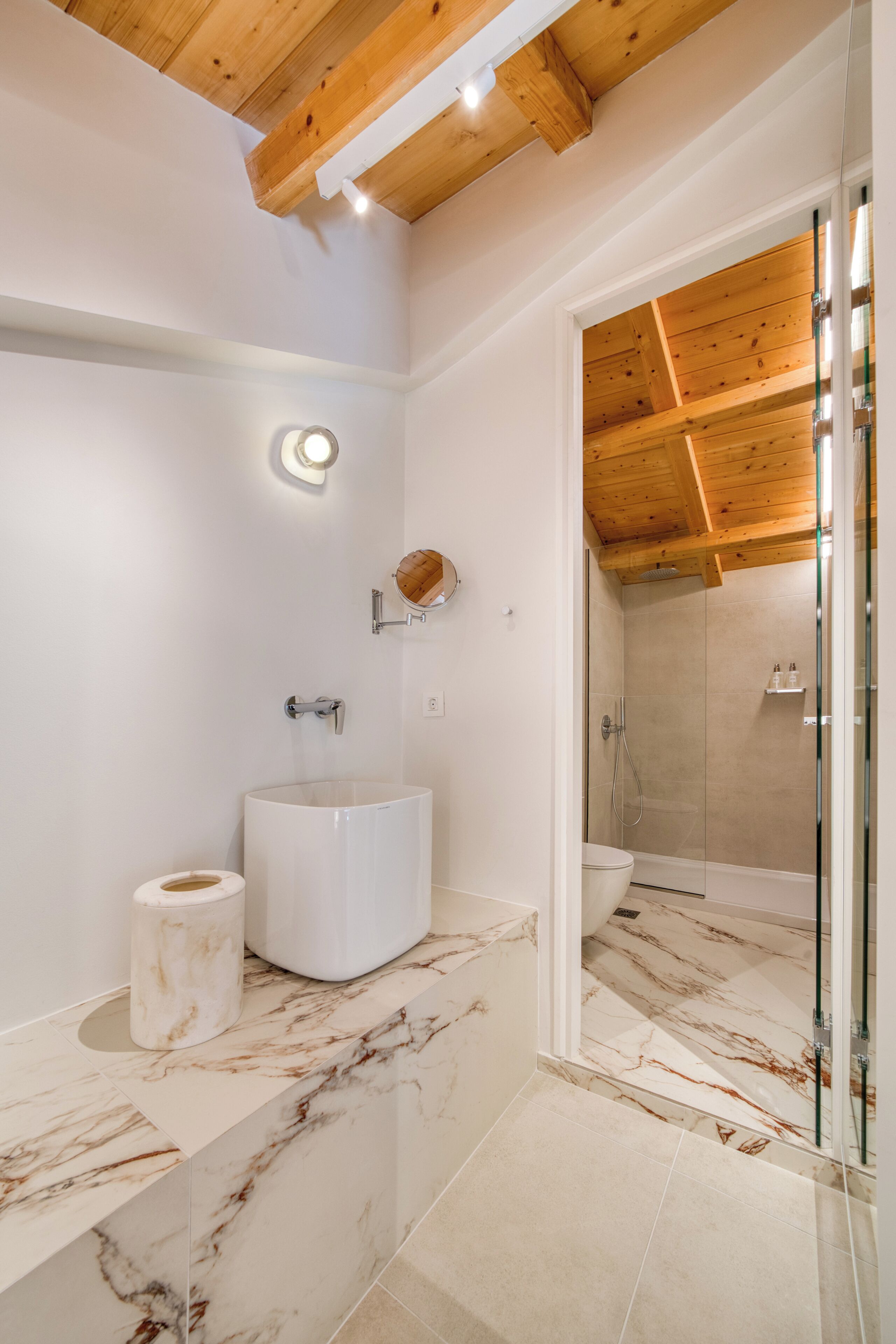 A modern bathroom with a marble sink, a toilet, and a glass-enclosed shower.