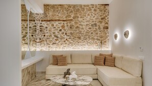 A modern living room with a stone wall, a beige sectional sofa, and a marble coffee table. - Nalia Suites (Nafplio)