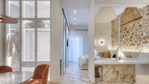 A modern hotel room with a marble floor, a round dining table with chairs, a large mirror, and a bed with a headboard. - Nalia Suites (Nafplio)