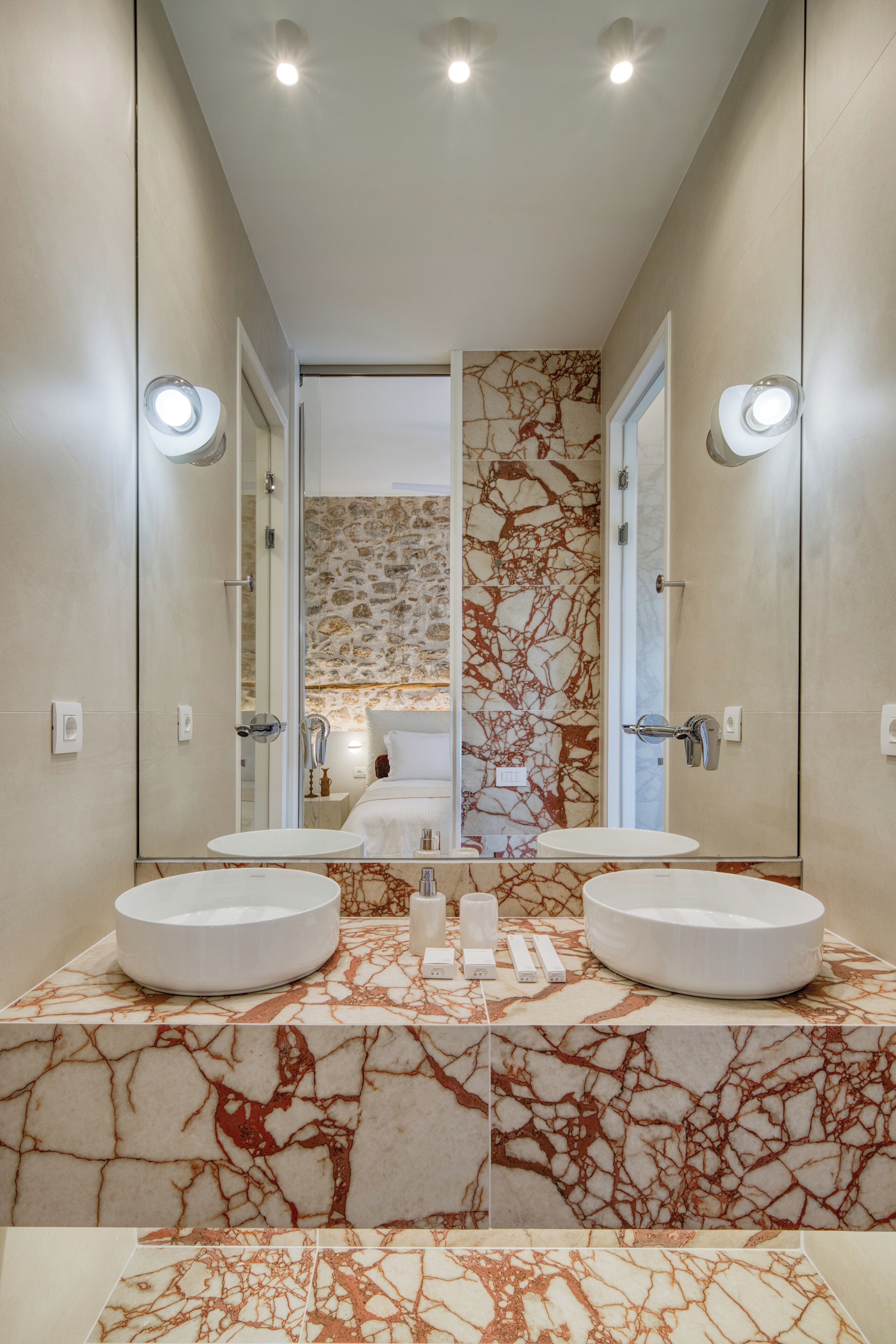 A modern bathroom with two round sinks, a marble backsplash, and a large mirror.