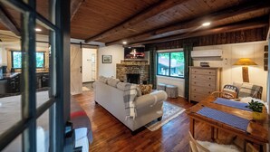 A cozy living room with a fireplace, wooden ceiling, and a dining area with a table and chairs. - Woodsman Lodge Property Buyout - Luxe Space for 41 ppl in Eureka! (Eureka Springs)