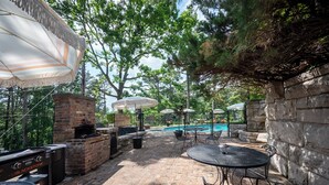 An outdoor patio with a brick fireplace, outdoor grill, and a pool area.