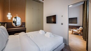 Ein modernes Hotelzimmer mit einem großen Bett, einem Kleiderschrank, einem Fernseher und einer Sitzecke mit einem Sessel.