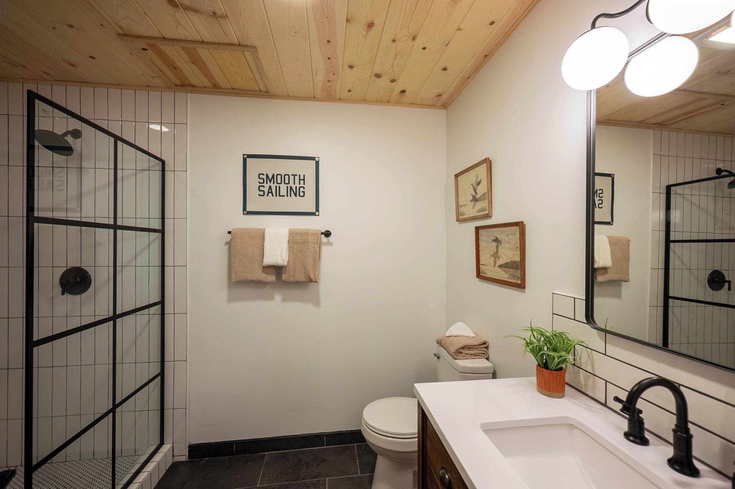 Une salle de bain moderne avec une douche à parois de verre, des toilettes, un lavabo avec un miroir et une pancarte sur laquelle on peut lire : « TOUT VA BIEN ».