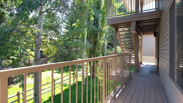 A wooden deck with a metal railing, surrounded by trees and a grassy area. - Après Haus Studio: Lock-off Unit w Pool, Hot Tubs, Sauna and Vail + BC Shuttle (Avon)