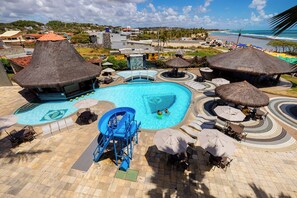 Zona de piscina en un resort con tobogán, sillas de descanso, sombrillas y vista al océano.