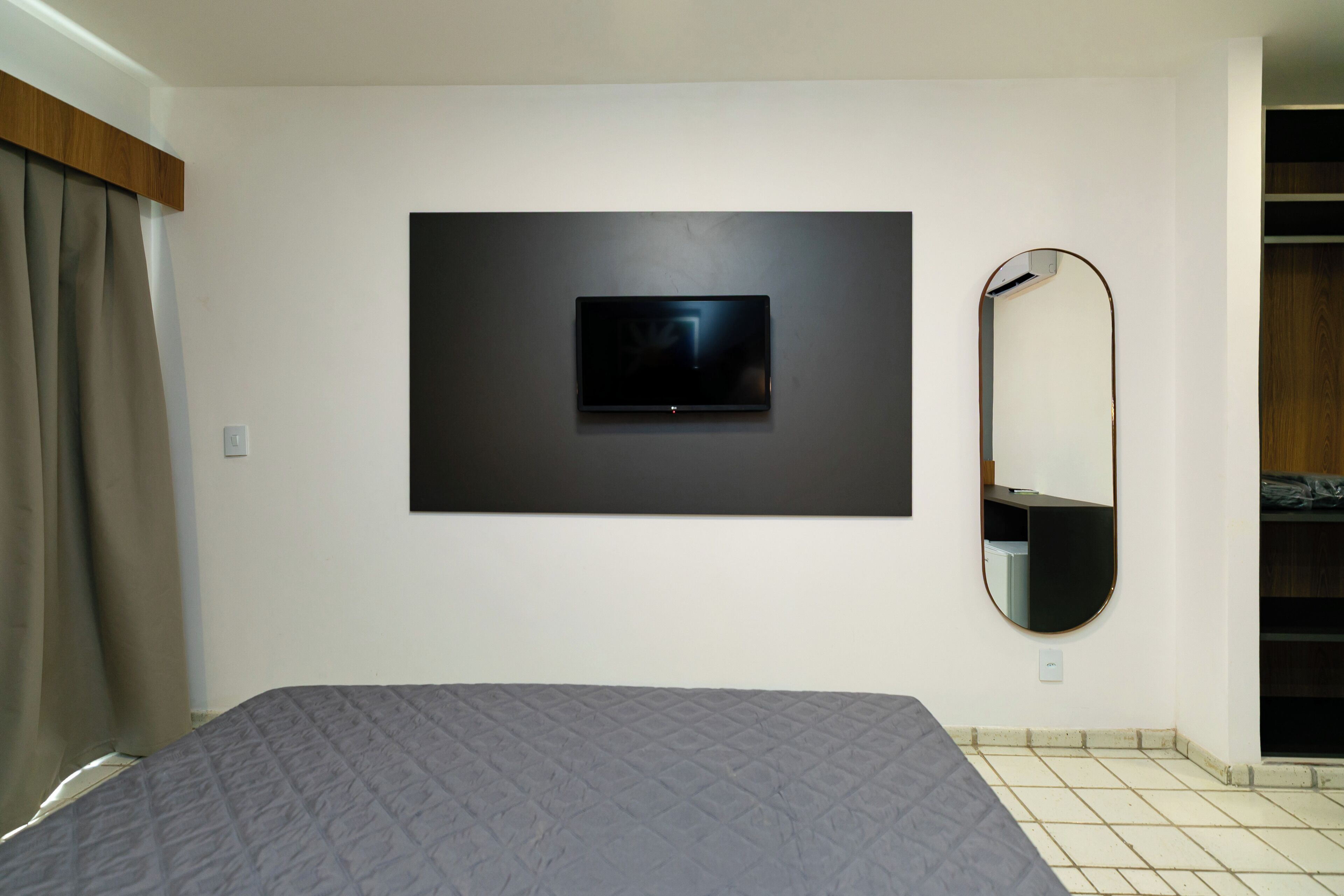 Quarto com cama, televisão na parede, espelho e guarda-roupa.